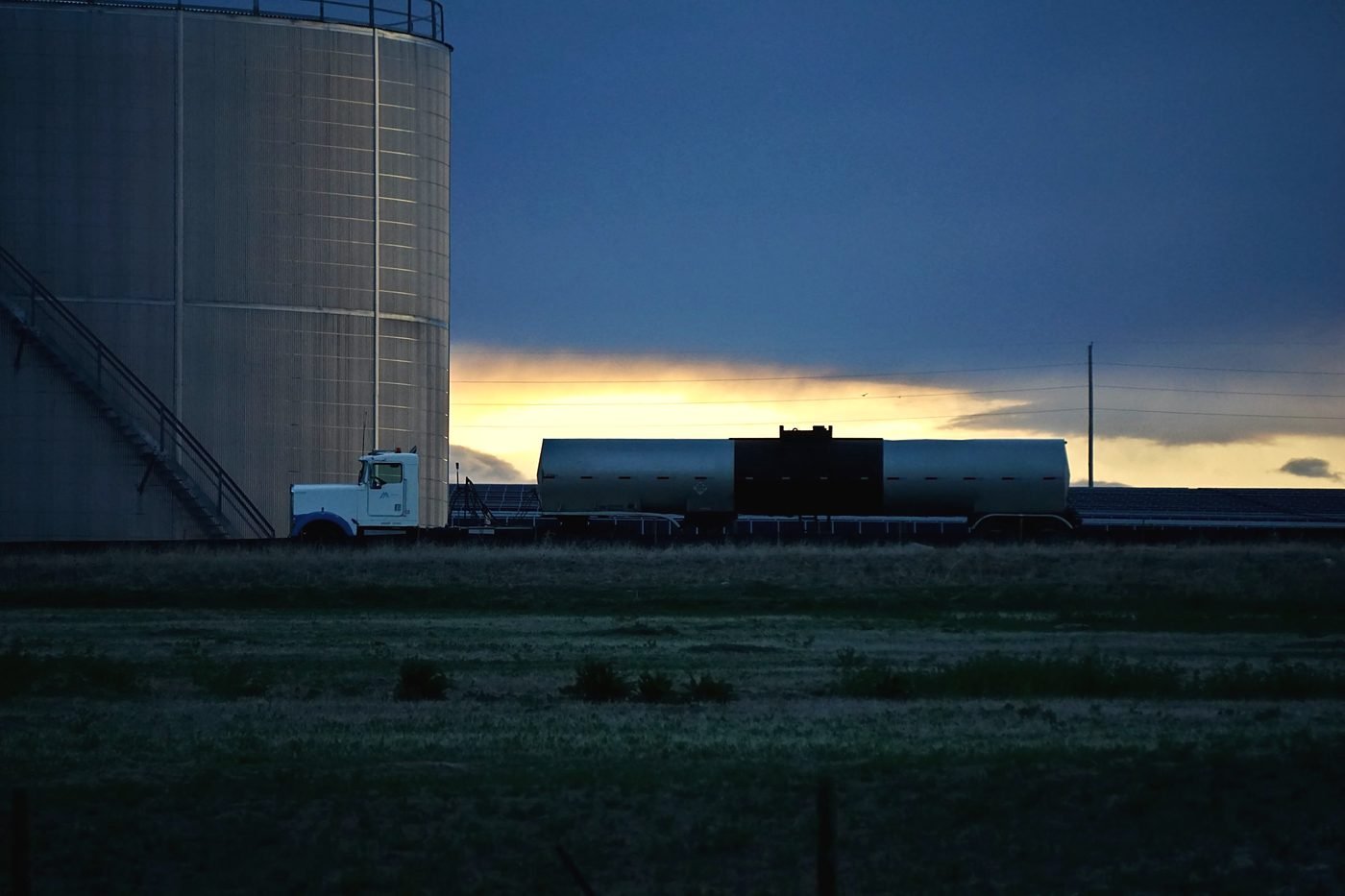 A tank truck beside bulk storage at dusk on the plains.